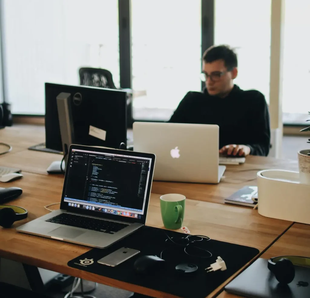 A web developer working on code in a modern office setting with multiple devices.